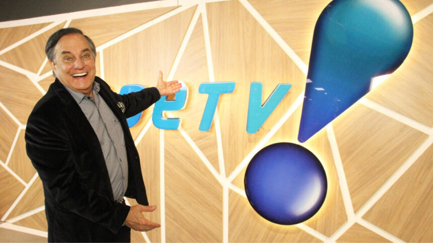 Ronnie Von apontando para o logo da RedeTV!, em uma parede na sede da emissora