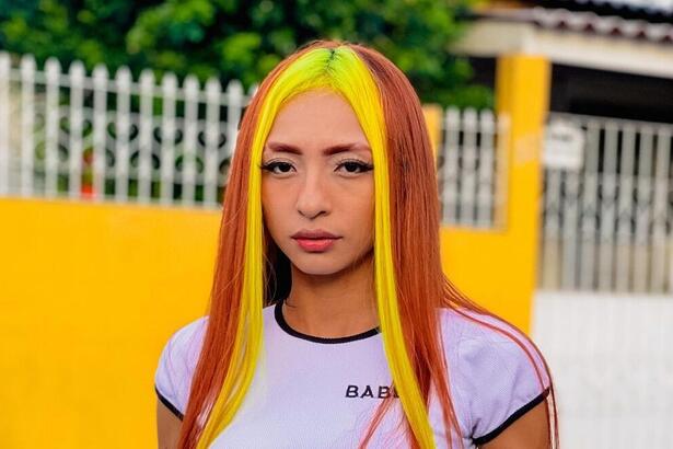 Ruivinha de Marte posando em frente a um portão, com mexas de cabelo amarelo e laranja