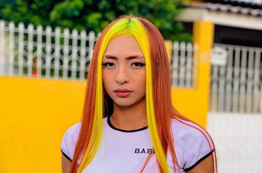 Ruivinha de Marte posando em frente a um portão, com mexas de cabelo amarelo e laranja