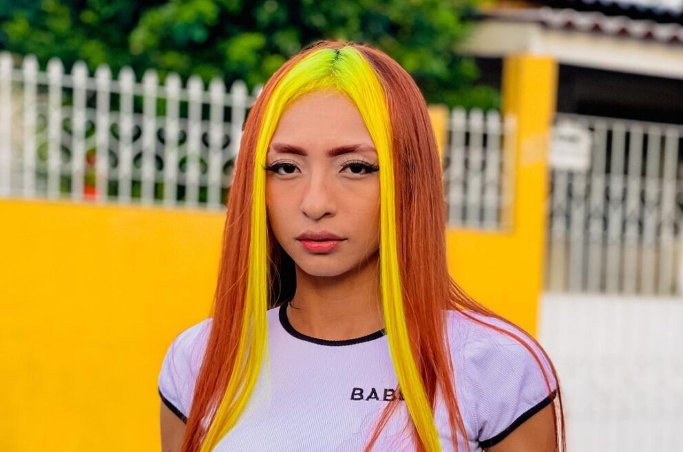 Ruivinha de Marte posando em frente a um portão, com mexas de cabelo amarelo e laranja