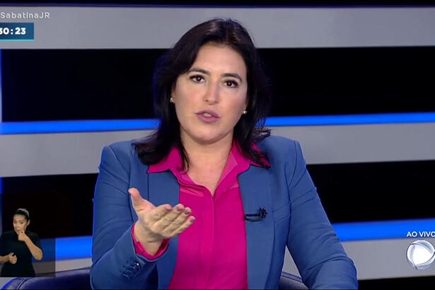 Simone Tebet de blazer azul, camisa social rosa, gesticulando durante entrevista na Record TV