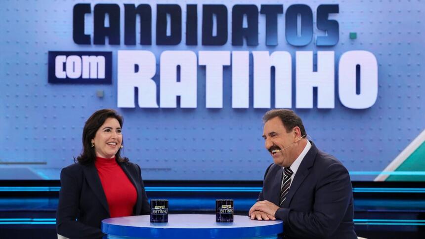 Simone Tebet de jaqueta preta, camisa vermelha, sorrindo, sentada em frente a Ratinho durante gravação do Candidatos com Ratinho, do SBT