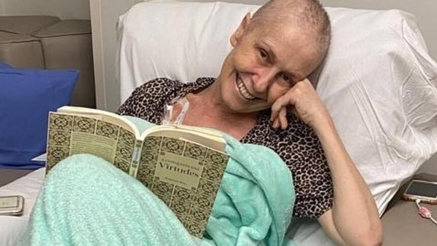 Susana Naspolini deitada em um leito de hospital, lendo um livro