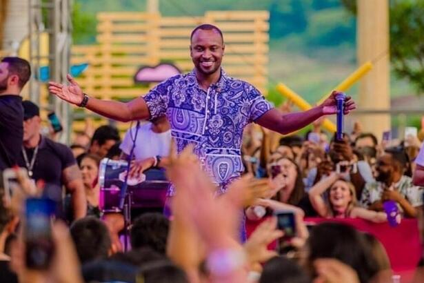 Thiaguinho sorrindo, de camisa roxa estampada, com braços abertos durante apresentação do Tardezinha