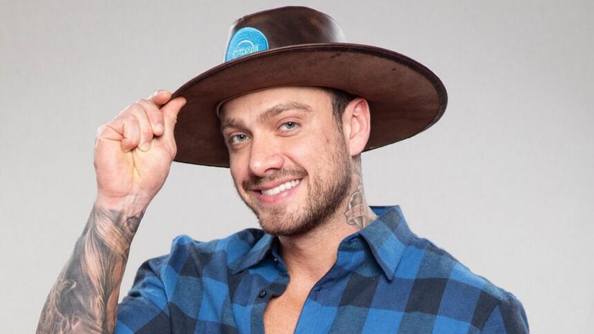 Vini sorrindo, segurando chapéu de fazendeiro de A Fazenda 14, da Record TV