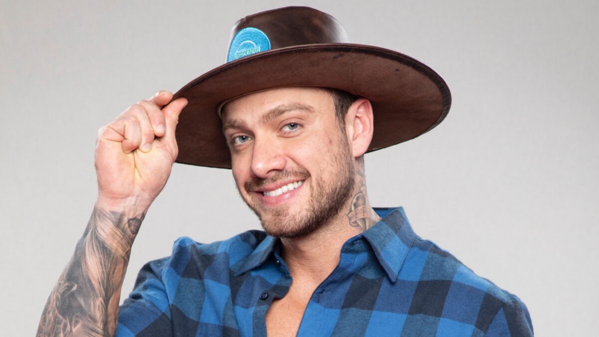Vini sorrindo, segurando chapéu de fazendeiro de A Fazenda 14, da Record TV