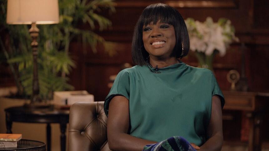 Viola Davis de camisa verde, sorrindo, de cabelo curto, liso, de franja, durante entrevista com Pedro Bial