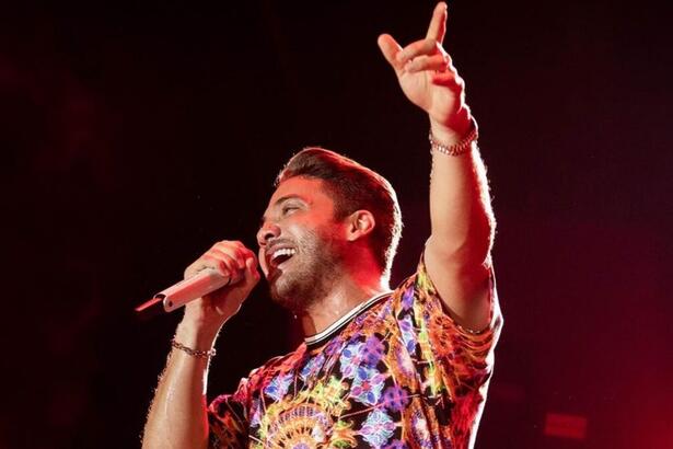 Wesley Safadão com camisa estampada colorida com o braço esquerdo levantado, apontando pra cima, segurando o microfone com a mão esquerda