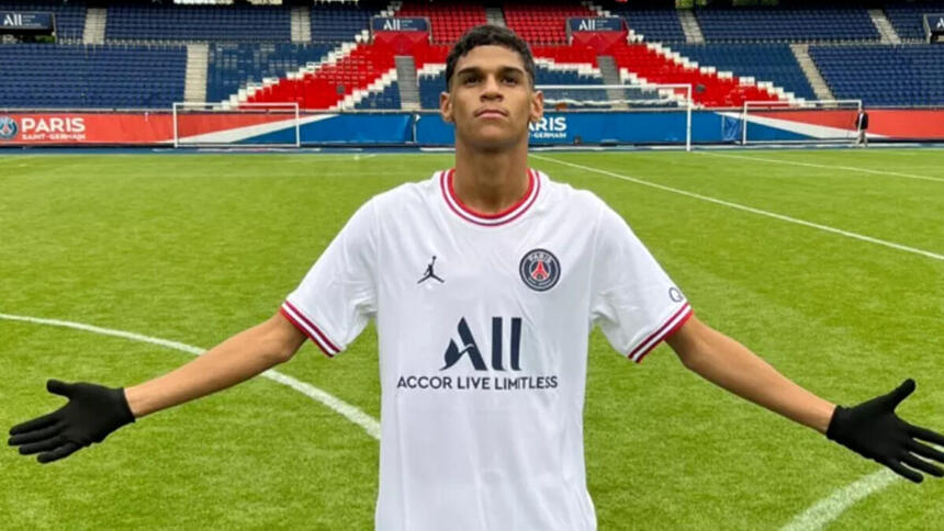 Luva de Pedreiro com os braços abertos com a camisa do PSG, no gramado do estádio Parque dos Príncipes