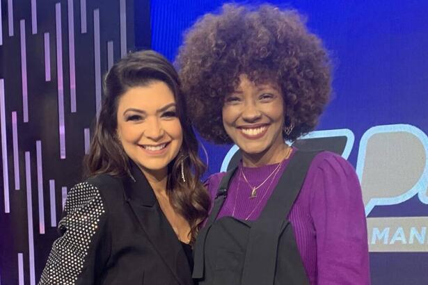 Amanda Françozo sorrindo ao lado de Isabel Filardis de macacão preto com camisa roxa durante gravação do De Papo com Amanda Françozo, da TV Aparecida