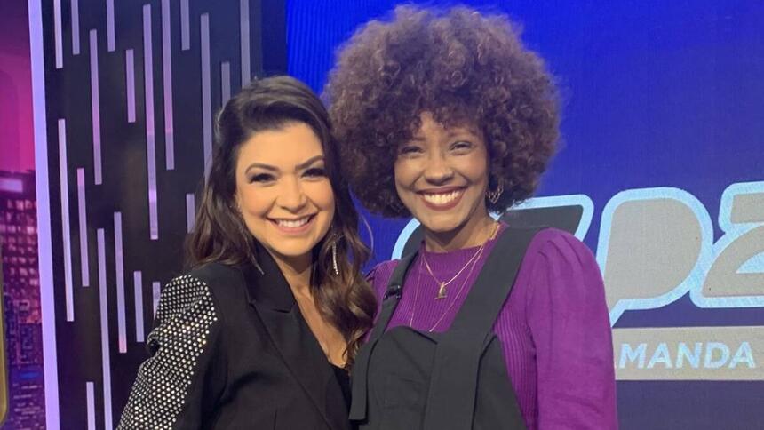 Amanda Françozo sorrindo ao lado de Isabel Filardis de macacão preto com camisa roxa durante gravação do De Papo com Amanda Françozo, da TV Aparecida