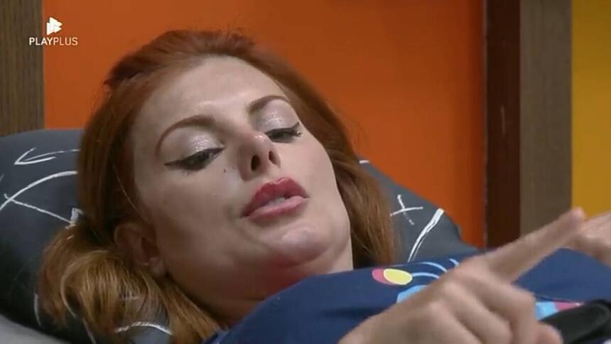 Deborah deitada na cama olhando para frente.