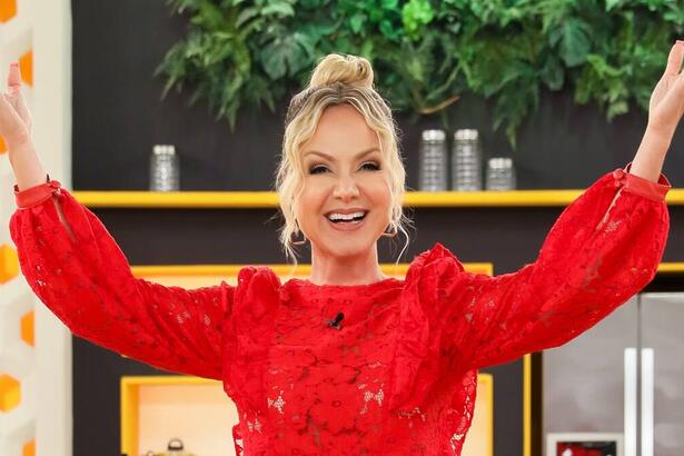 Eliana de top vermelho, cabelo preto, sorrindo com os braços abertos para cima durante gravação do seu programa no SBT