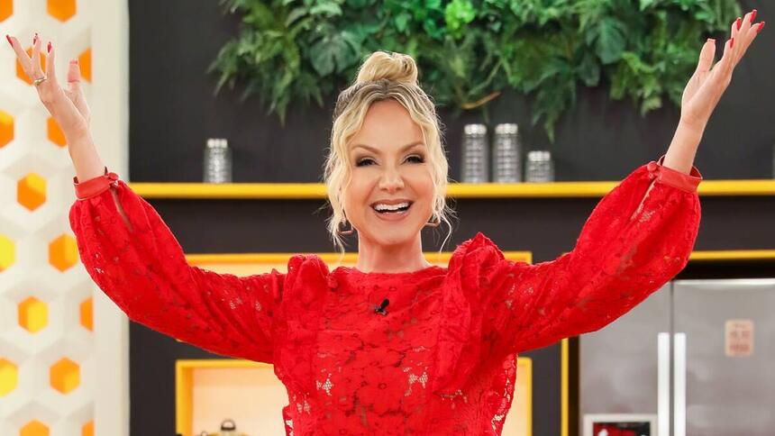 Eliana de top vermelho, cabelo preto, sorrindo com os braços abertos para cima durante gravação do seu programa no SBT