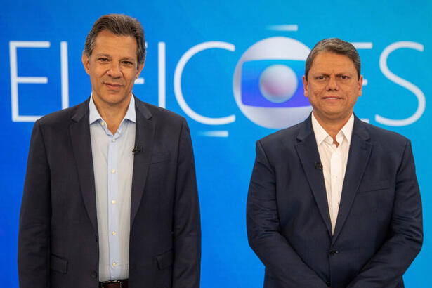 Fernando Haddad e Tarcísio de Freitas posados em frente ao telão, no cenário do debate de 2º turno na TV Globo