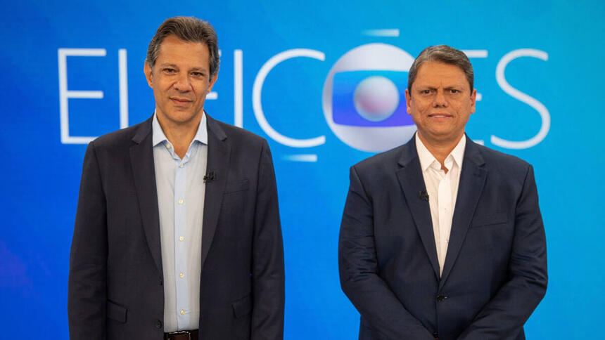 Fernando Haddad e Tarcísio de Freitas posados em frente ao telão, no cenário do debate de 2º turno na TV Globo