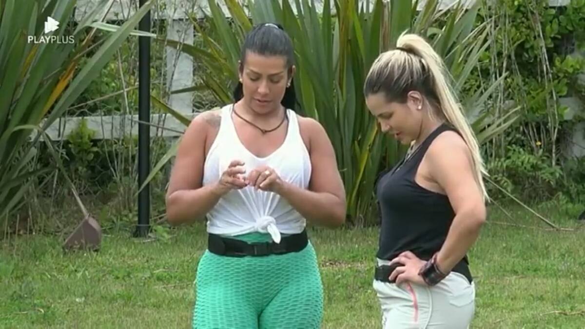 Moranguinho de camiseta branca em em pé ao lado de Deolane que se encontra com a mão na cintura e olhando para baixo.