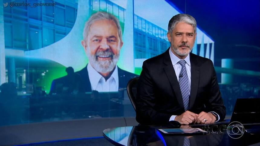 William Bonner sentado na bancada com Lula na projeção do Jornal Nacional, da TV Globo