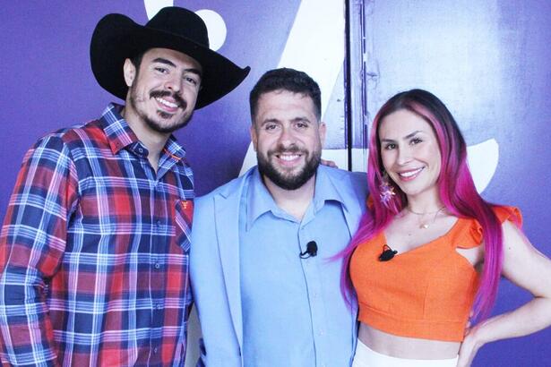 Jacques Vanier de chapéu de vaqueiro, camisa estampada quadriculada, sorrindo, ao lado de Mauricio Meirelles de blazer e camisa social azul ao lado Emme White de camisa laranja e saia branca