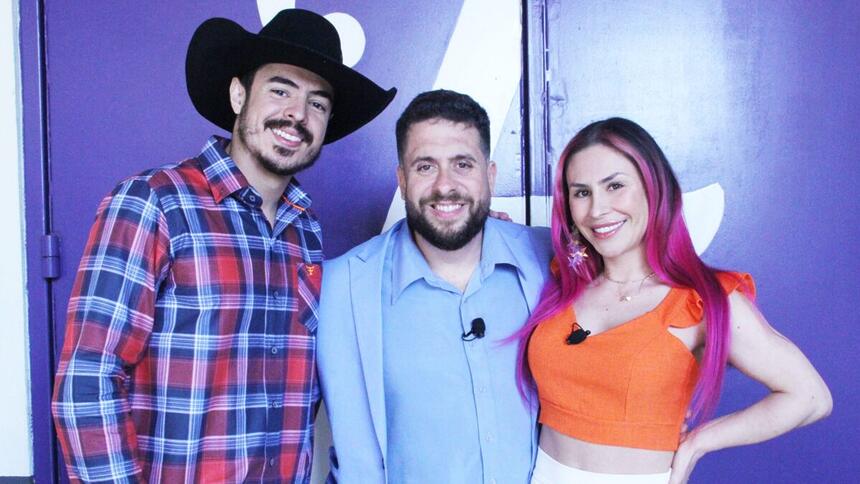 Jacques Vanier de chapéu de vaqueiro, camisa estampada quadriculada, sorrindo, ao lado de Mauricio Meirelles de blazer e camisa social azul ao lado Emme White de camisa laranja e saia branca