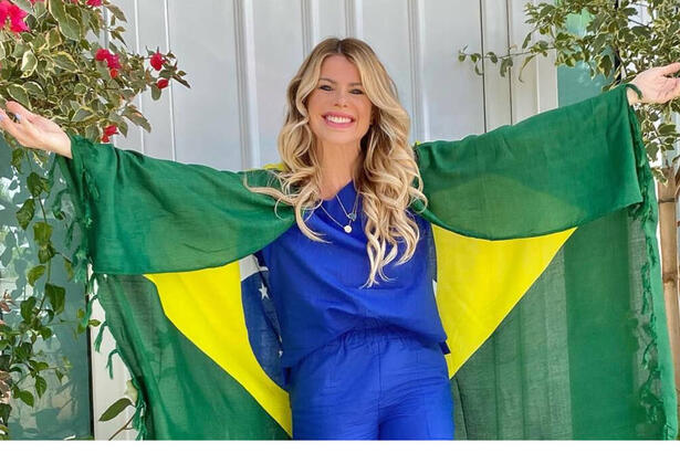 Karina Bacchi com os braços abertos e uma bandeira do Brasil nos ombros