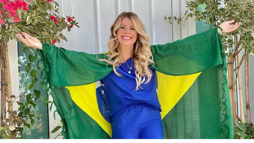 Karina Bacchi com os braços abertos e uma bandeira do Brasil nos ombros