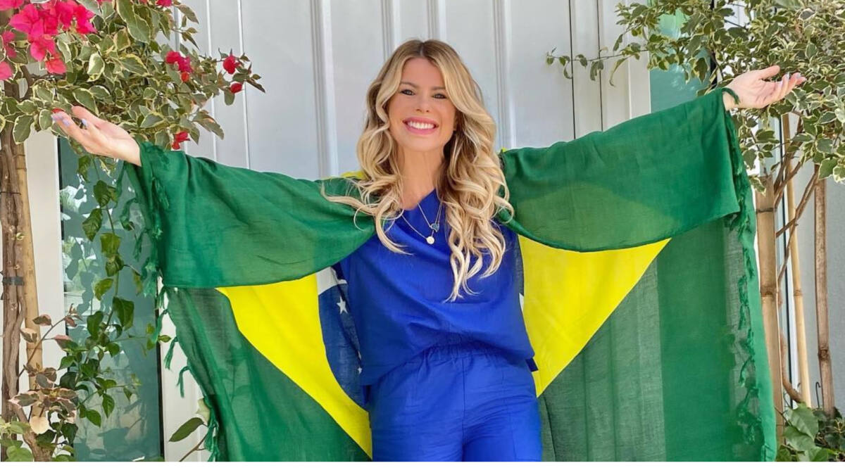 Karina Bacchi com os braços abertos e uma bandeira do Brasil nos ombros