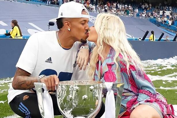 Éder militao e Karoline Lima se beijando e segurando uma taça conquistada pelo atleta, em campo pelo Real Madrid