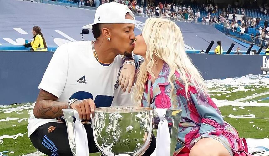 Éder militao e Karoline Lima se beijando e segurando uma taça conquistada pelo atleta, em campo pelo Real Madrid