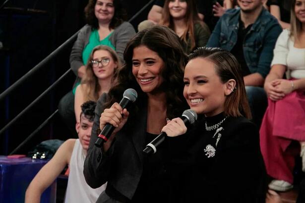 Isadora Cruz de look preto sorrindo ao lado de Larissa Manoela durante gravação do Altas Horas, da TV Globo