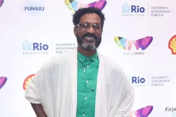 Luis Miranda de manta branco, camisa social verde, de oculos de grau, sorrindo, com as mãos na cintura durante passagem pelo Festival do Rio