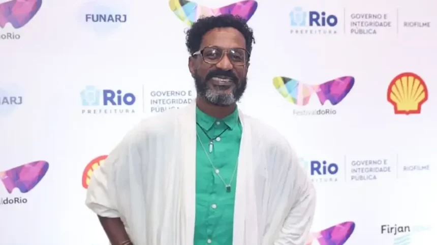 Luis Miranda de manta branco, camisa social verde, de oculos de grau, sorrindo, com as mãos na cintura durante passagem pelo Festival do Rio