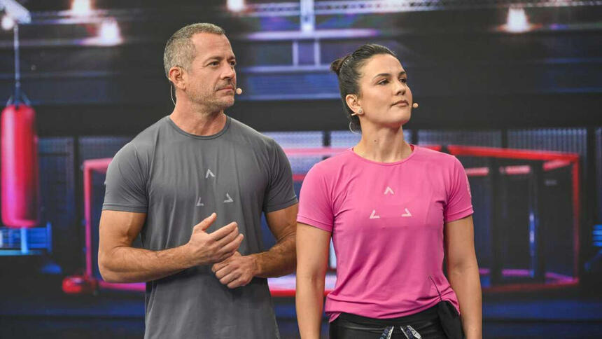 Malvino Salvador de camisa cinza, sério; Kyra Gracie de camisa rosa, semblante sério durante gravação do Faustão na Band