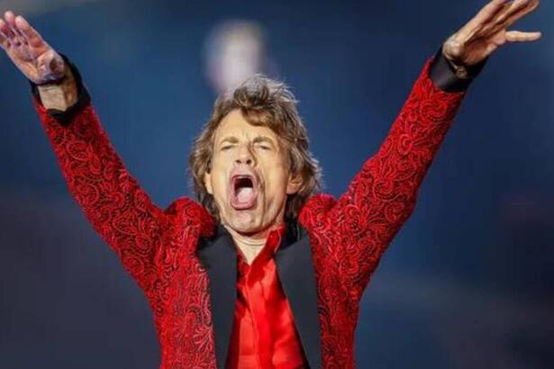 Mick Jagger com as mãos levantadas vestido de vermelho