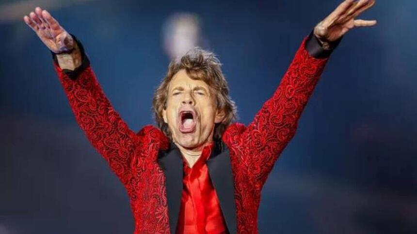 Mick Jagger com as mãos levantadas vestido de vermelho