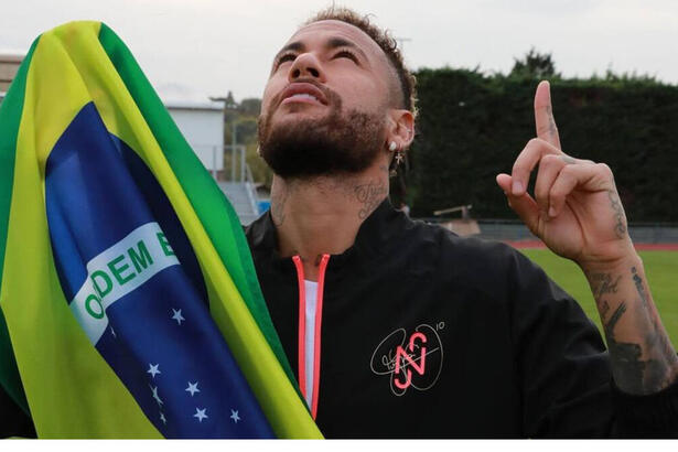 Neymar segurando uma bandeira do Brasil e apontando os dedos para o alto