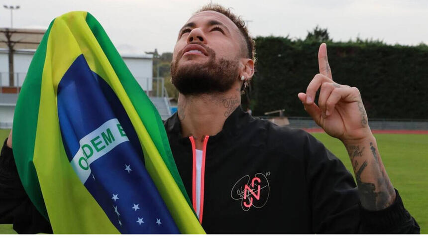 Neymar segurando uma bandeira do Brasil e apontando os dedos para o alto