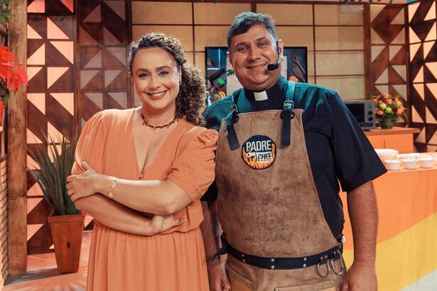 Padre Chef Evandro e Letícia Andrade de vestido marrom, sorrindo, com braços cruzados durante gravação de Sabor de Vida, da TV Aparecida