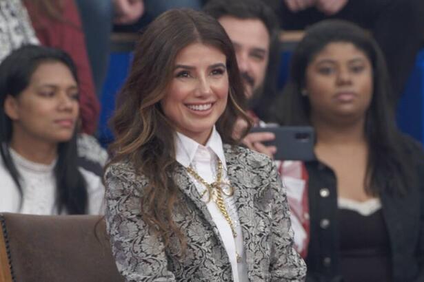 Paula Fernandes de blazer e camisa social sorrindo, sentada, durante gravação do Altas Horas