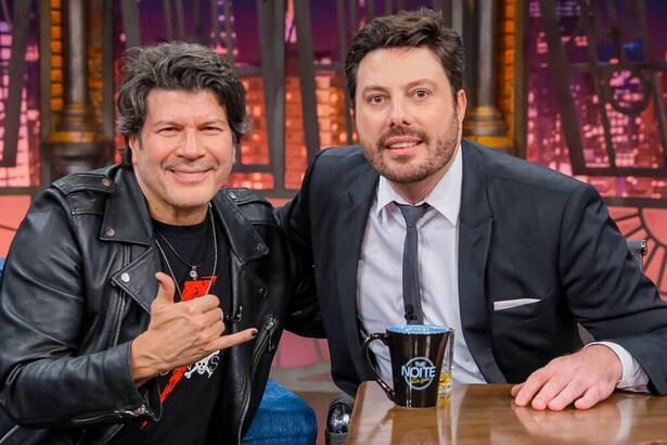 Paulo Ricardo de jaqueta de couro preta, sorrindo, sentado ao lado de Danilo Gentili durante gravação do The Noite, do SBT