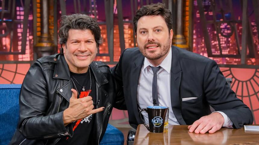 Paulo Ricardo de jaqueta de couro preta, sorrindo, sentado ao lado de Danilo Gentili durante gravação do The Noite, do SBT