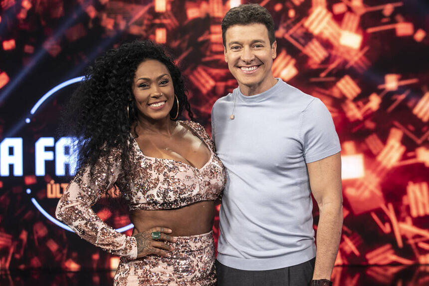 Rosiane Pinheiro com top e saia estampada em bege, marrom, sorrindo, ao lado de Rodrigo Faro durante gravação do Hora do Faro da Record TV