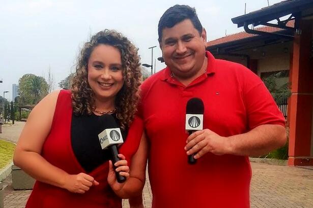 Padre Chef Evandro e Letícia Andrade de vestido marrom, sorrindo, segurando microfone com a mão esquerda durante gravação de Sabor de Vida, da TV Aparecida em homenagem a Nossa Senhora Aparecida