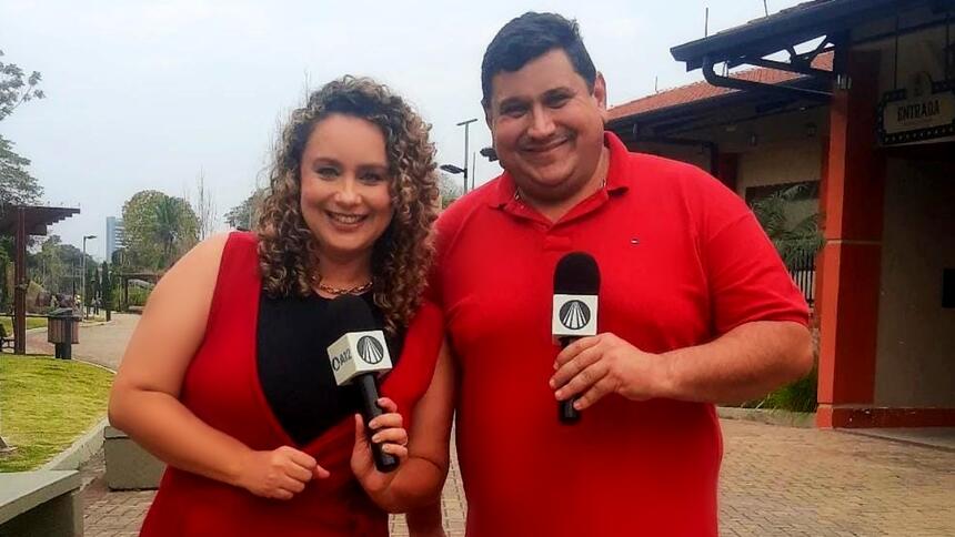 Padre Chef Evandro e Letícia Andrade de vestido marrom, sorrindo, segurando microfone com a mão esquerda durante gravação de Sabor de Vida, da TV Aparecida em homenagem a Nossa Senhora Aparecida