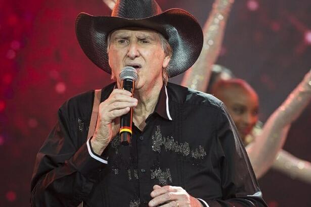 Sergio Reis de camisa e chapéu de cowboy pretos cantando durante gravação do Faustão na Band