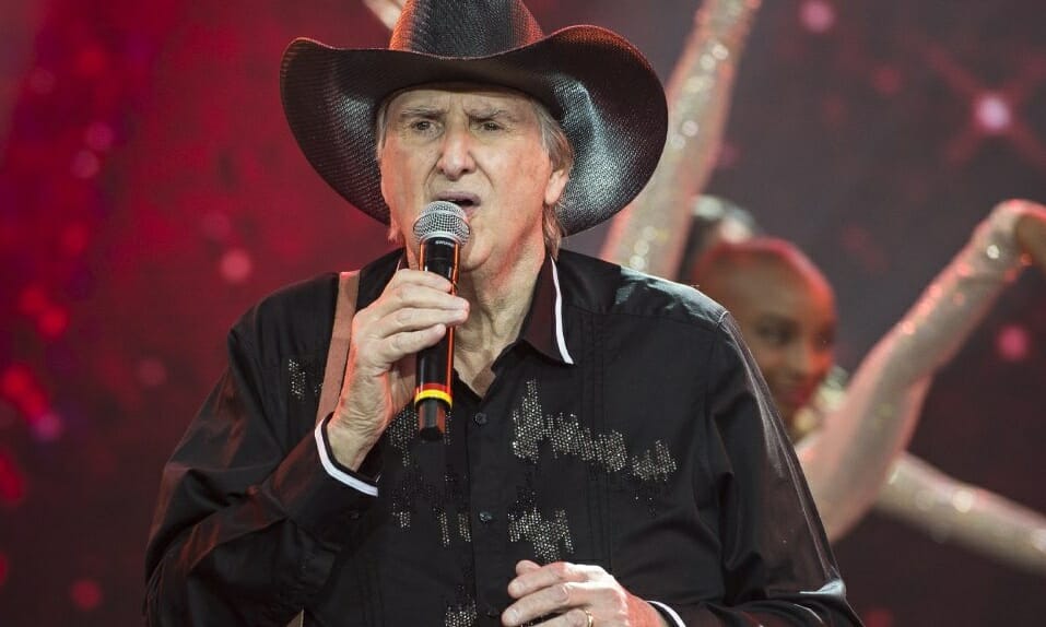 Sergio Reis de camisa e chapéu de cowboy pretos cantando durante gravação do Faustão na Band