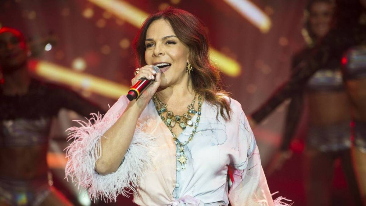 Sula Miranda com camisa mangalonga e pluma na manda segurando o microfone com a mão direita durante gravação do Faustão na Band