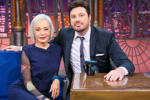 Tânia Alves de vestido azul escuro, sentada ao lado de Danilo Gentili durante gravação do The Noite, do SBT