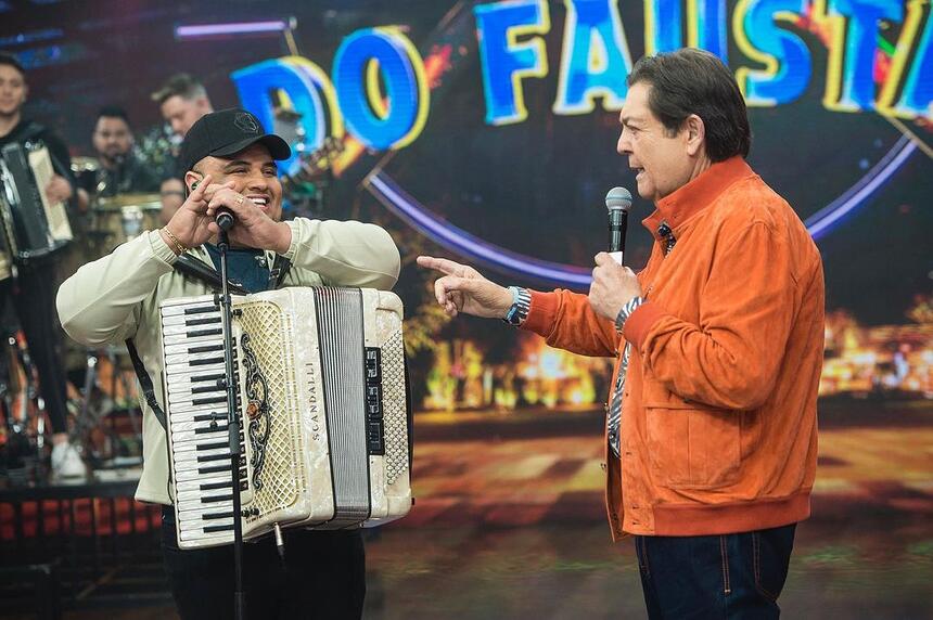 Tarcisio do acordeon com safona branca, segurando microfone durante gravação do Faustão na Band