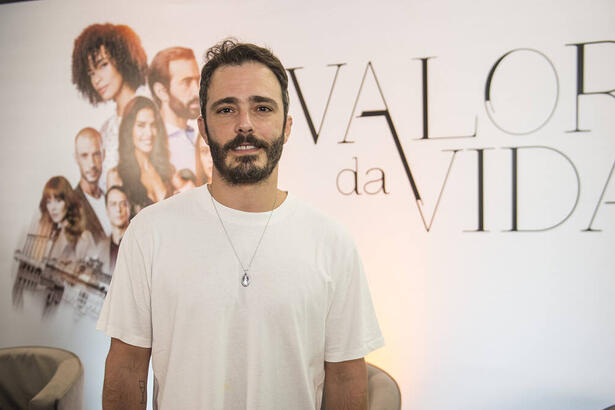 Ator Thiago Rodrigues em foto posada, na frente do banner de divulgação da novela Valor da Vida, na Band